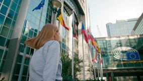 Back view of Woman Walking along EU Flags to European Parliament Office in Brussels, Belgium. Politics, Economy and Business Concept. 4K gimbal follow low angle shot in slow motion - Powered by Shutterstock - Get 15% off with code: PIKWIZARD15