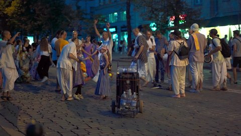 Kharkov, Ukraine August 2021 Hare Krishna devotees playing musical instruments, dancing and singing main city street at night. People walking around Holiday evening crowd Handheld effect