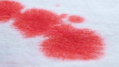 Red blood drops on a white bandage, paper or cloth-like surface. Splattering red color of blood, bloodstains reveal on white background. Shallow depth of field. Macro view.