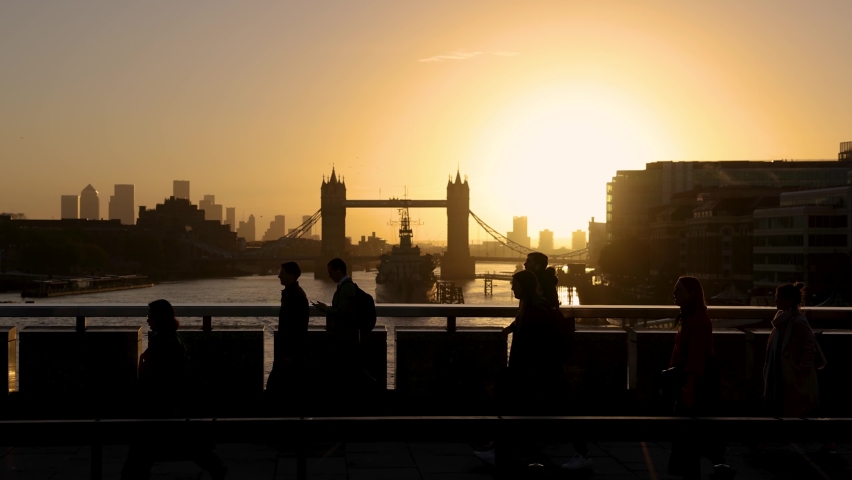 London, United Kingdom - October 25th 2021: morning rush hour with people in silhouette going to work during sunrise in front of the Tower Bridge and skyline
