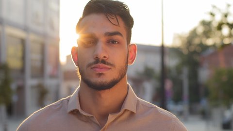 Portrait male calm serious face outdoors on street in city sunlight background. Hispanic arabic bearded guy business man successful entrepreneur standing outside looking at camera in sunbeams sunset