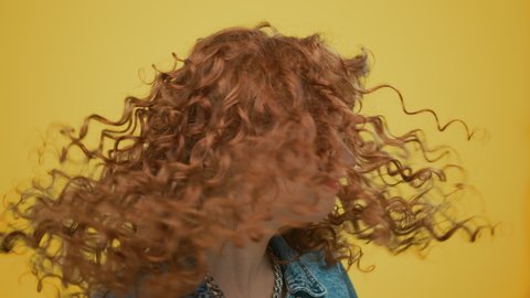 Positive woman waving head on yellow background. Portrait of redhead girl moving head with curly hair in slow motion. Closeup happy girl turning head in studio. Female fashion model smiling camera