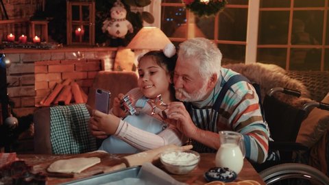Little teenager takes a selfie photo with her grandfather. People with disabilities at home for the holidays. The concept of cake preparation and fun at home for Christmas Arkivvideo