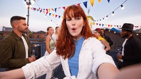 Young caucasian woman making video with her friends on a party using smartphone. Rooftop party friends having fun, singing and dancing together.