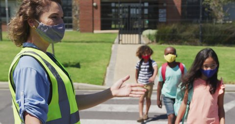 Female woman wearing hi vis vest helping group of kids wearing face masks to cross the road