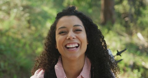 Portrait of smiling biracial woman in forest during hiking in countryside. healthy, active lifestyle and outdoor leisure time.