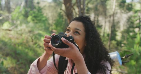 Smiling biracial woman taking photo in forest during hiking in countryside. healthy, active lifestyle and outdoor leisure time.