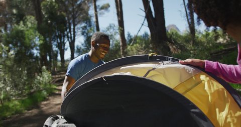 Smiling diverse couple preparing tent at camp in countryside. healthy, active lifestyle and outdoor leisure time.