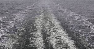 View of the wake behind a large passenger ferry at sea on a cloudy autumn morning. White foam trail behind the ship created by the motion of the ship