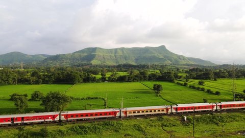 Igatpuri - Maharashtra, India. September 6, 2021: Aerial footage of countryside with a railway train passes the landscape. Translation on train "Indian Railways, AC First Tier,  Sleeper."
