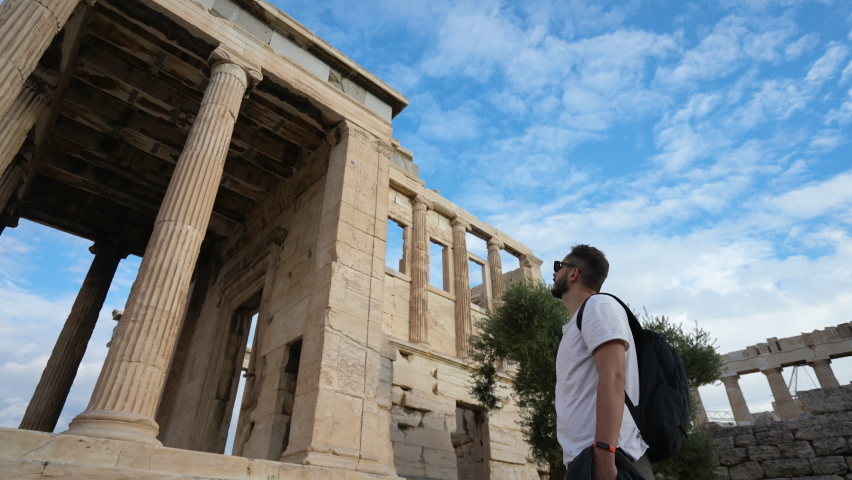 Tourist among pillars of ancient temple spends time on touristical looking around, mesmerized by Greek shrine architecture. Traveler on sight of Acropolis in Athens. Tourism, traveling to old ruins.