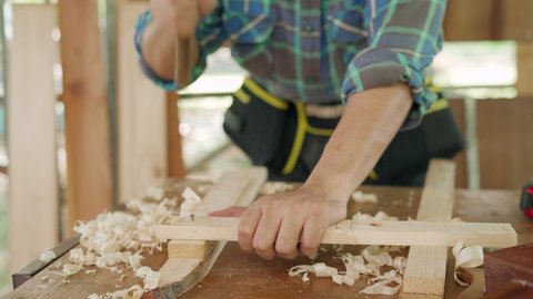 Asian man who owns a small lumber business is process for furniture production. A carpenter is using a hammer to drive nails to hold the wood together. home furniture concept.