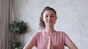 Online yoga training with skilled practitioner. Positive woman in pink t-shirt greets followers holding hands spbi in namaste mudra at home camera view 4k video
