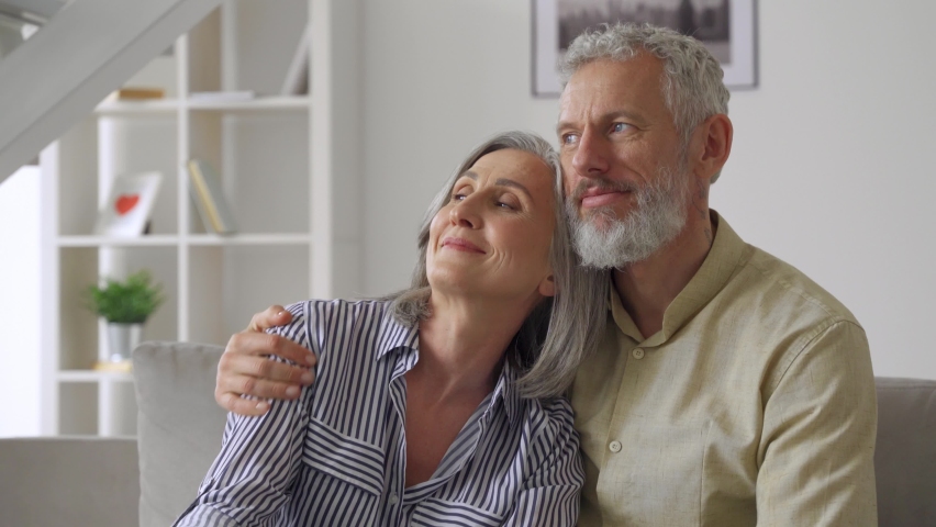 Happy affectionate mature adult husband embracing kissing wife enjoying tender moment or love and care. Middle age 50s romantic grey haired married couple bonding together, hugging at home. Royalty-Free Stock Footage #1081453529