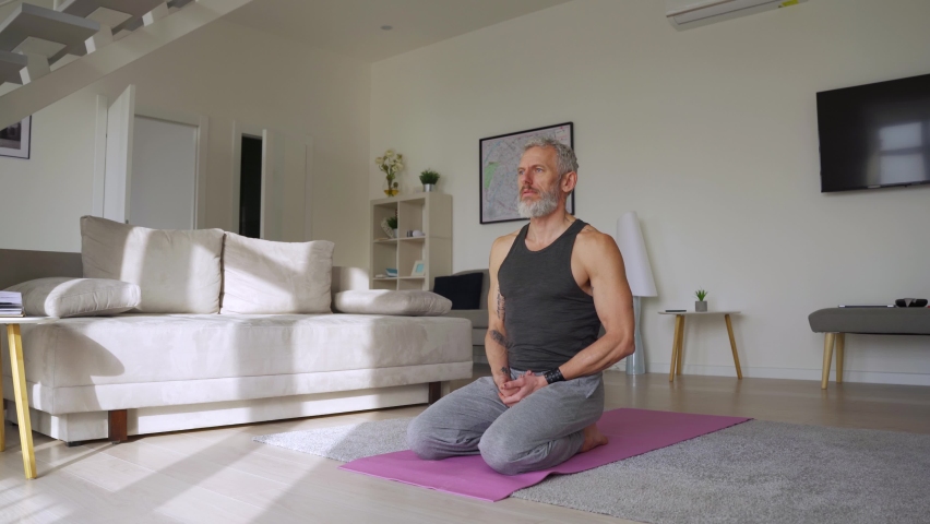 Fit healthy sporty active tattooed senior mature mid age hipster man doing morning workout exercise at home, enjoying sport pilates yoga fitness training breathing on mat in modern living room. Royalty-Free Stock Footage #1081453538