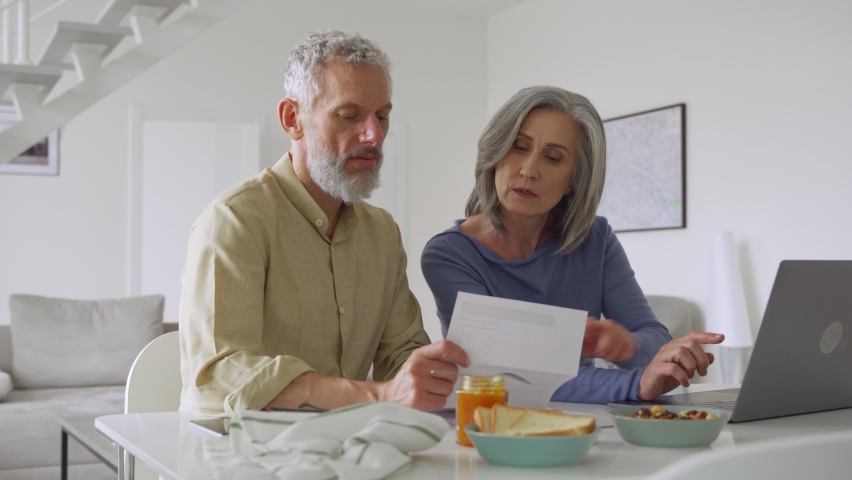 Senior middle aged couple holding financial documents paper bills paying bank loan online, calculating pension fees, payments, taxes, planning family retirement money finances using laptop at home. Royalty-Free Stock Footage #1081453562