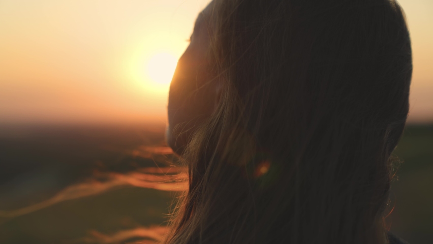 Young girl looks at sunset and prays, religious person, her hair is flying in wind in glare of the sun, to believe in goodness, a woman's dream of love, to think and ask for forgiveness from heaven | Shutterstock HD Video #1081456067