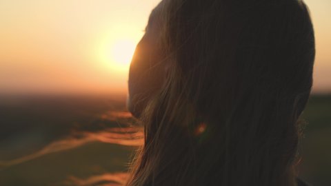 young girl looks at sunset and prays, religious person, her hair is flying in wind in glare of the sun, to believe in goodness, a woman's dream of love, to think and ask for forgiveness from heaven