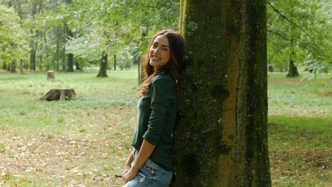 Smiling woman leaning on tree trunk in park