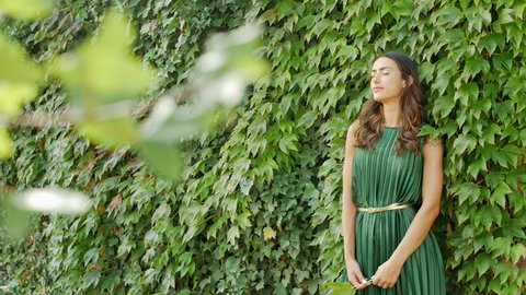 Woman in green summer dress leaning on overgrown wall