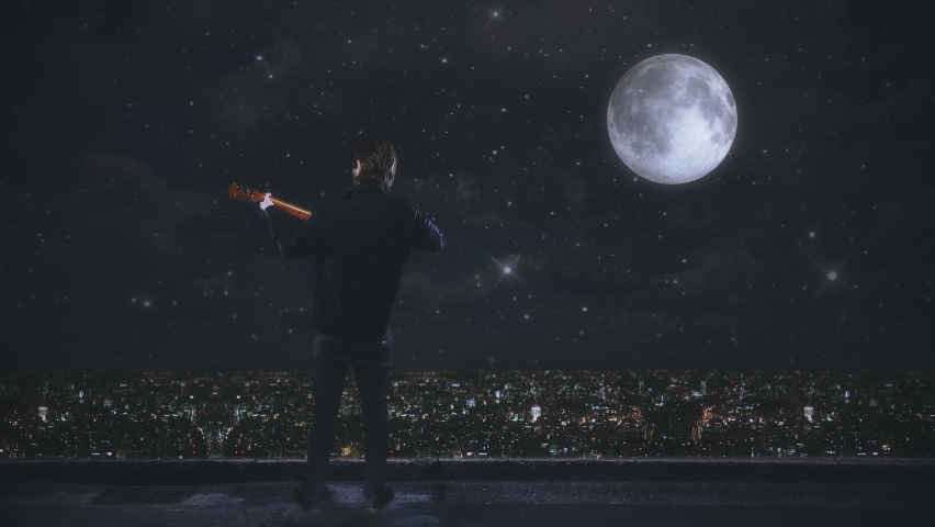 Musician Playing Guitar Over City Night Under Moonlight. Male musician playing acoustic guitar under moonlight on top of a building with city view at night