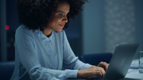 Successful African American Businesswoman Working on Laptop Computer in Big City Office Late in the Evening. Female Executive Manager Analyzing Financial Reports, Marketing Research and Plans.