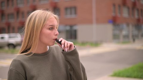Close-up of a smoking woman in the city. Young woman sadly inhales smoke and looks in front of her