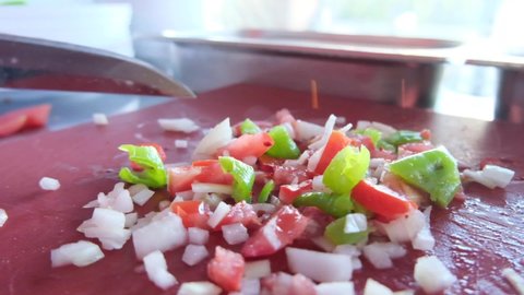 Pieces of tomatoes, peppers, onions chopped with a knife on a red countertop.Salad preparation process slow motion