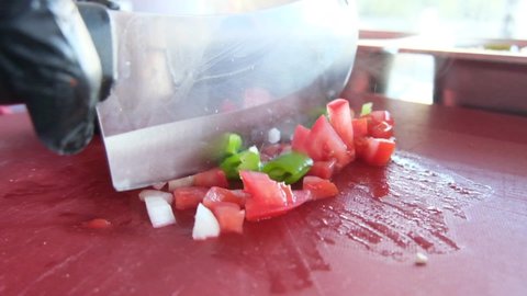 Pieces of tomatoes, peppers, onions chopped with a knife on a red countertop.Salad preparation process slow motion