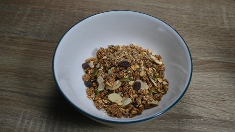 Granola in a bowl a spoon digs in and Almond Milk being poured in making bubbles, seeds, dried fruits, raisins, healthy breakfast.
