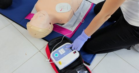 CPR training medical procedure workshop. Demonstrating chest compressions and use of AED automatic defibrillator on CPR doll