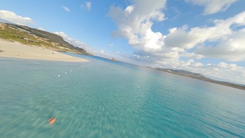 FPV video, view from above, flying at high speed over a turquoise water with a beautiful  white sand beach La Pelosa Beach, Stintino,. Sardinia, Italy.