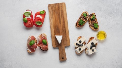 Stop motion animation of cooking open sandwiches with mozzarella, camembert, ham, mushrooms, tomatoes, basil. Bruschetta set for wine