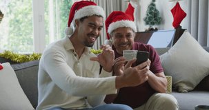 Happy biracial son with father in santa hats doing video call on smartphone in christmas. christmas, festivity and communication technology.