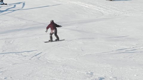 Slow-motion shot of skilled snowboarder extremely carving down the slope at high speed on a sunny winter day at a ski resort. Snowboard buttering tricks.