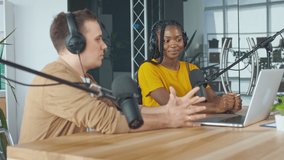 Confident African American Woman With White Man Hosting a Podcast About Music During a Radio Show in a Modern Studio. Conversation Into a Microphone in a Broadcast Studio. Podcast Concept.
