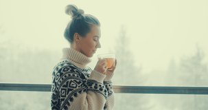 Woman in knitted wool sweater drinks tea a cup, relax on terrace at home in winter day. Health care, authenticity, sense of balance and calmness. Fresh air, It's Snow time. 4K Video	