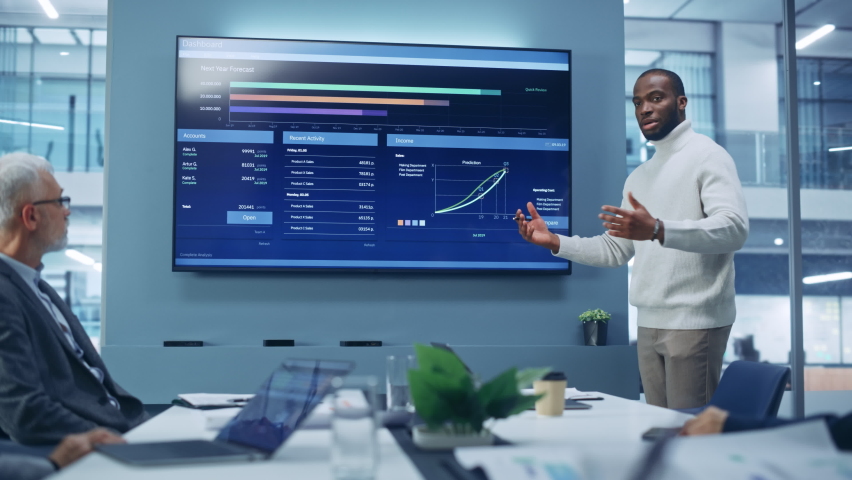 Diverse Modern Office: Motivated Black Businessman Leads Business Meeting with Managers, Talks, uses Presentation TV with Statistics, Charts, Big Data. Digital Entrepreneurs Work on e-Commerce Project Royalty-Free Stock Footage #1081470401