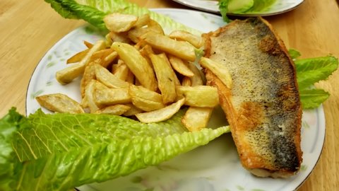 Home cooking - Rotating around serving plates of cooked walleye or Yellow Pike fillet and fried French fries with lettuce decoration.