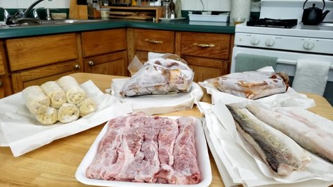 Home cooking - Panning right to left of lot of air sealed and or frozen food like fish, pork, beef and some croquettes battered in breadcrumbs thawing before cooking.