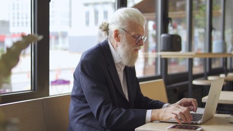 Modern elderly male editing text on laptop, working in cafe, online education