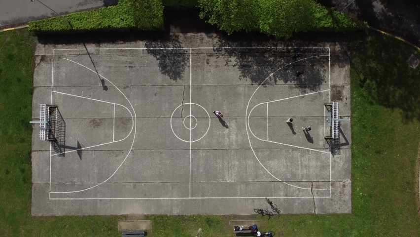 People playing basketball on a city court in the park in Mortsel, near Antwerp. Nice shadows over the players as this is a drone top down aerial shot
