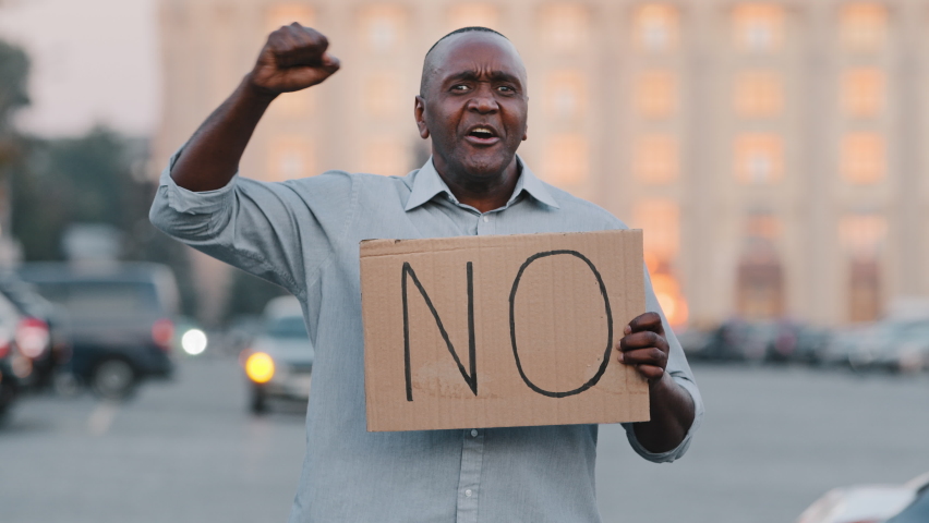 Stop concept. Black African American man protests against discrimination showing protest sign on strike. Protester immigrant person holding cardboard slogan banner with text no. Political unrest Royalty-Free Stock Footage #1081486586