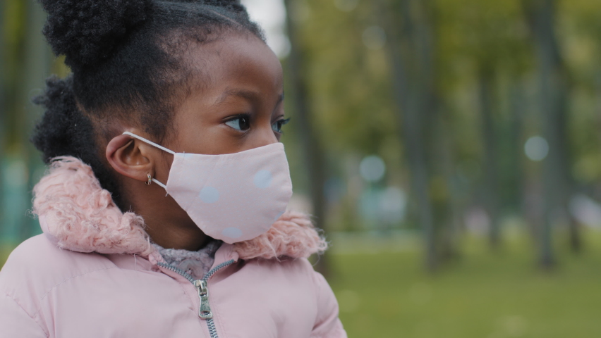Close up kid face little girl in medical mask looks away turning head looking at camera in city street. Portrait of masked child baby pupil schoolgirl posing in park pandemic coronavirus quarantine Royalty-Free Stock Footage #1081486697