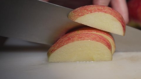 This close up video shows chef hands slices a juicy fresh apples with a knife on a cutting board.