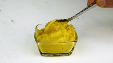 Spicy mustard scoop up with spoon, from glass bowl, for eating. Preparation fast tasty spicy food.