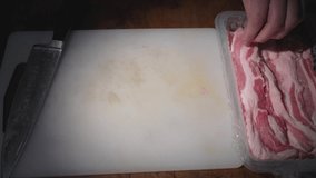This real time video shows an anonymous hand taking fresh pork belly bacon meat from a package and putting it on a cutting white gel board in preparation to make a recipe.