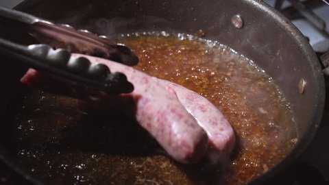This video shows bratwurst sausage link meat being placed in a boiling hot pan of oil by chef tongs in slow motion.