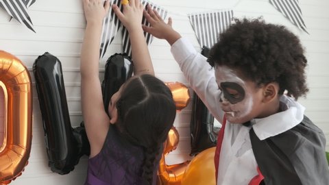 Little girl and boy in costume witch and dracula decorated wall for halloween party together. 