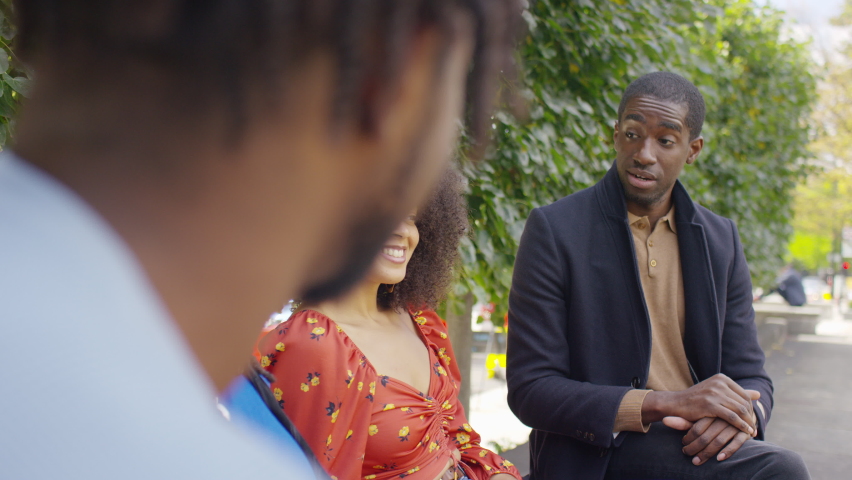 Group of friends or family sat together engaging in conversation on a bench outdoors in the city